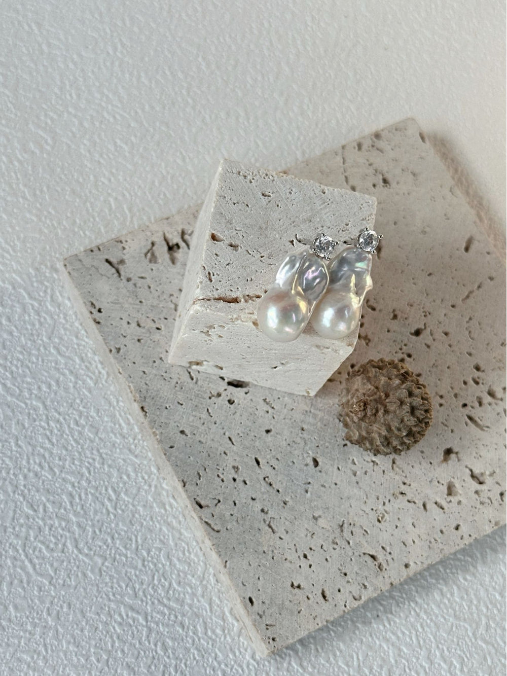 Baroque pearl earrings with sparkling accents displayed on textured background tile