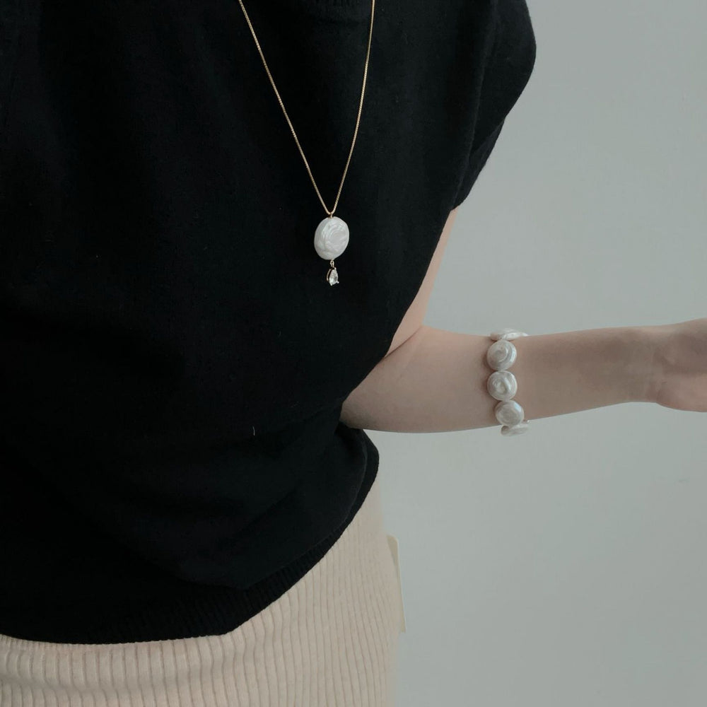 Elegant disc baroque necklace featuring a unique pendant, worn with a stylish black top and matching bracelet