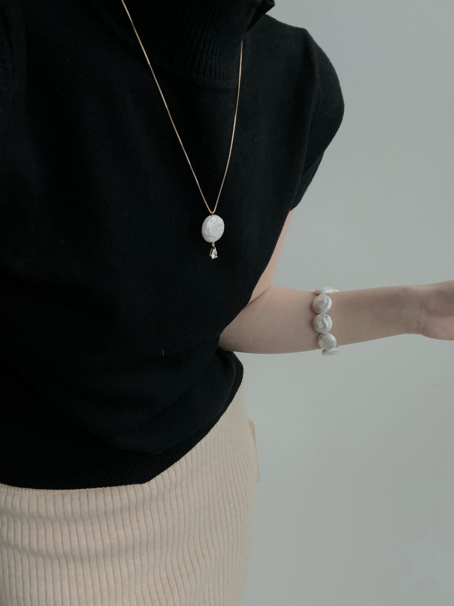 Elegant disc baroque necklace featuring a unique pendant, worn with a stylish black top and matching bracelet