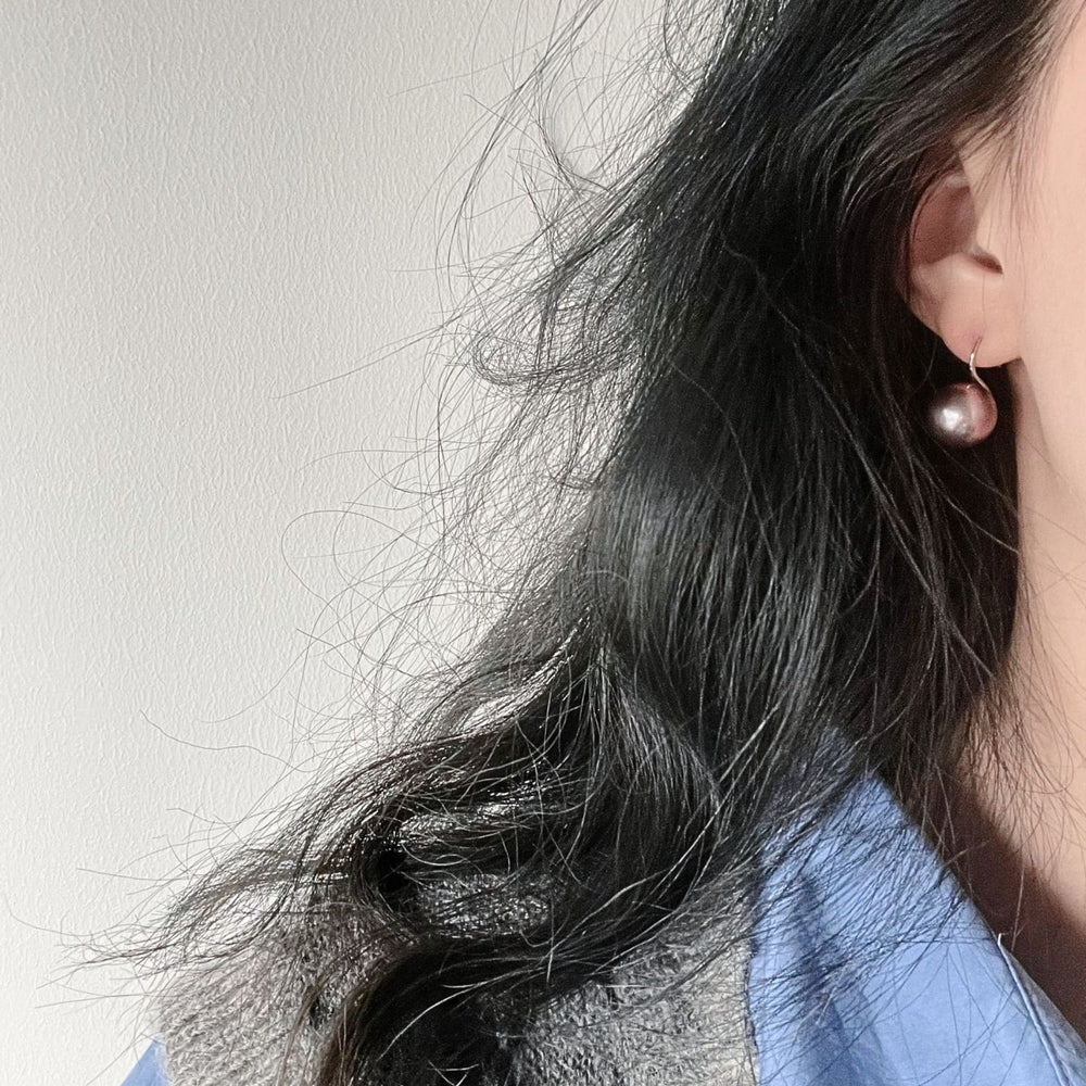 Elegant pearl earrings showcased on a model with wavy hair wearing a blue shirt