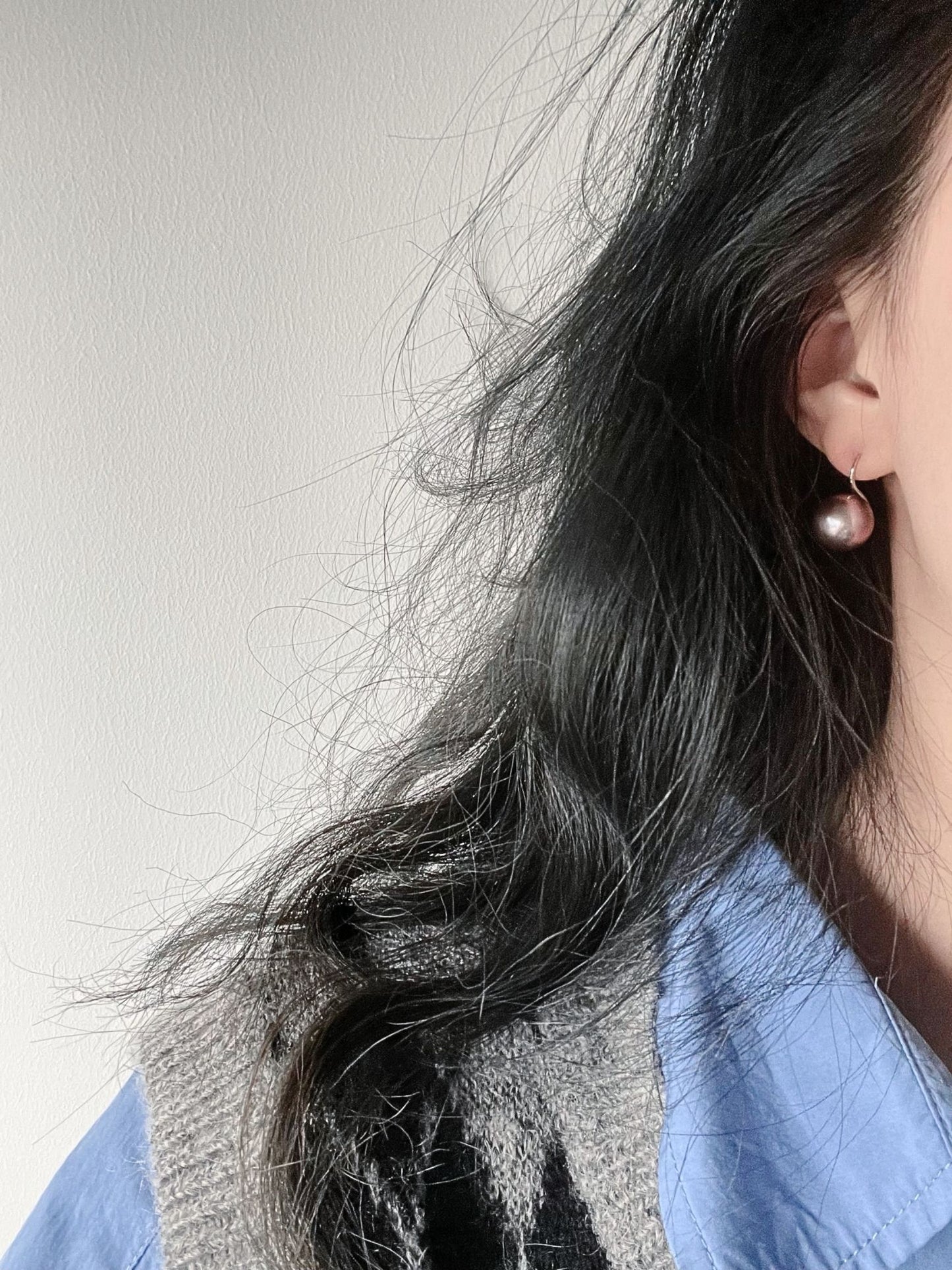 Elegant pearl earrings showcased on a model with wavy hair wearing a blue shirt