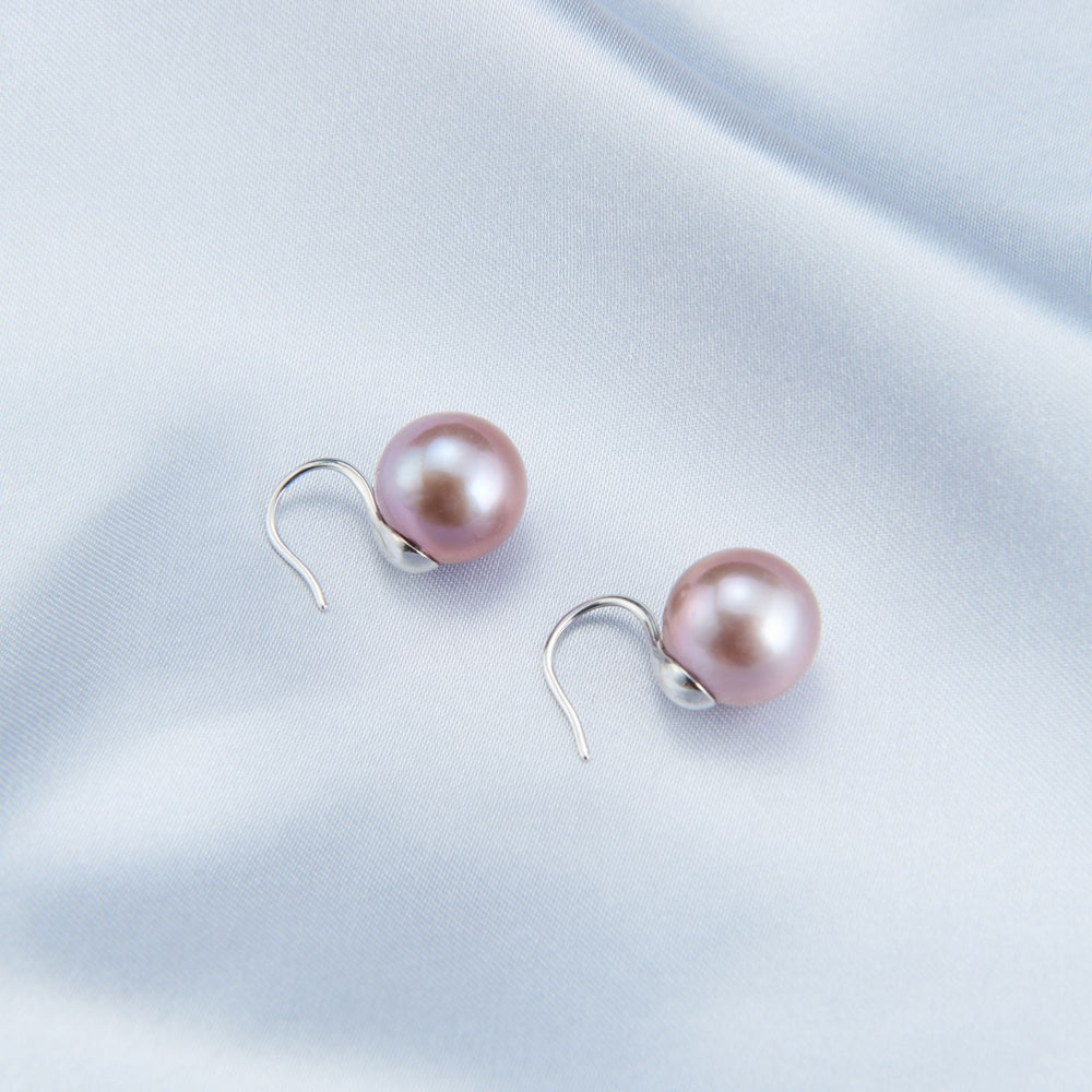 
                      
                        Elegant pearl earrings with a soft pink hue and silver hooks on smooth satin fabric
                      
                    
