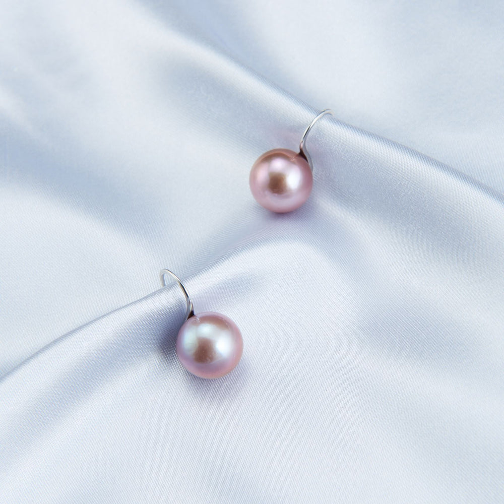 Elegant pearl earrings with pink pearls on a soft blue satin fabric background