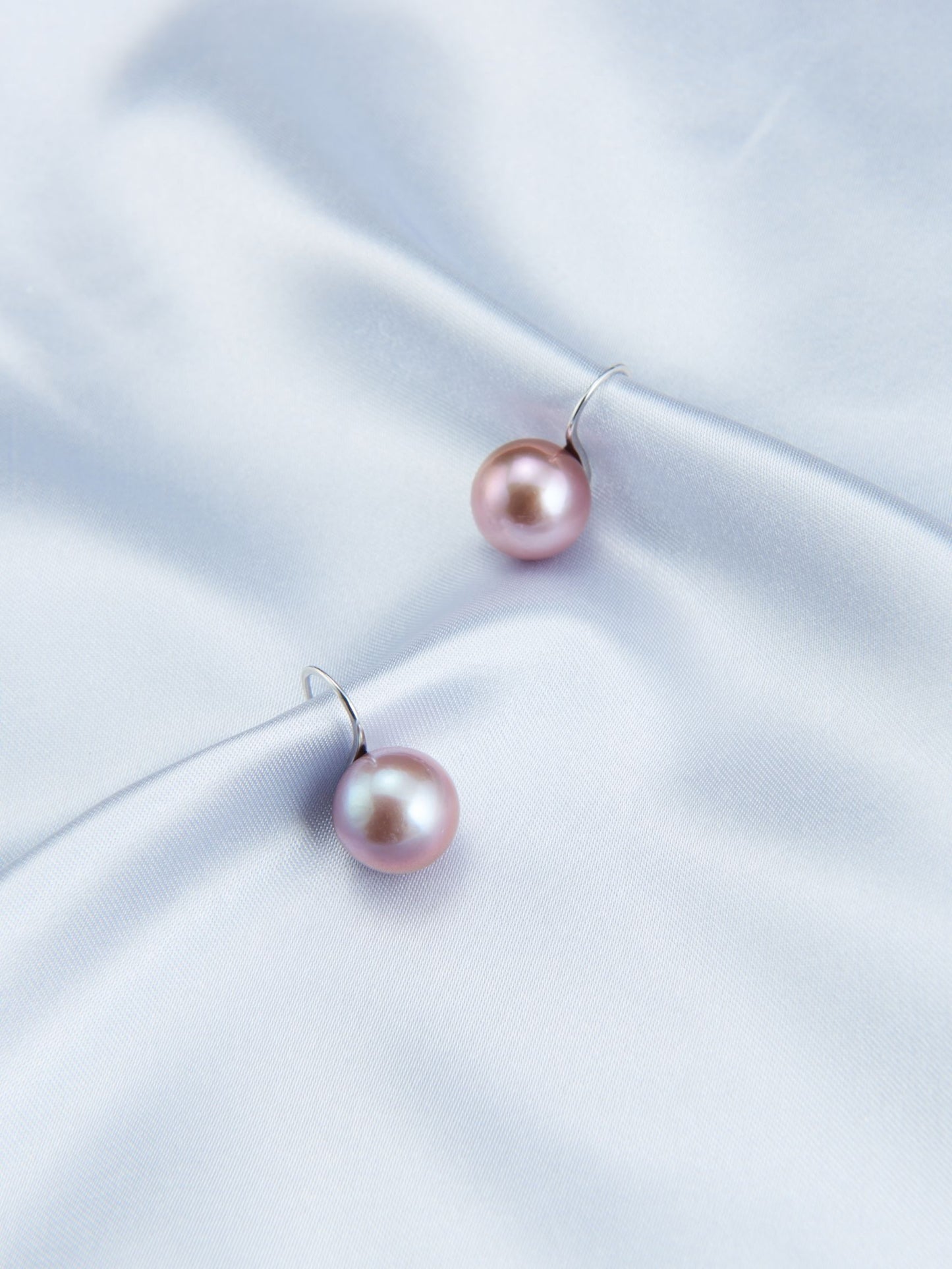 Elegant pearl earrings with pink pearls on a soft blue satin fabric background