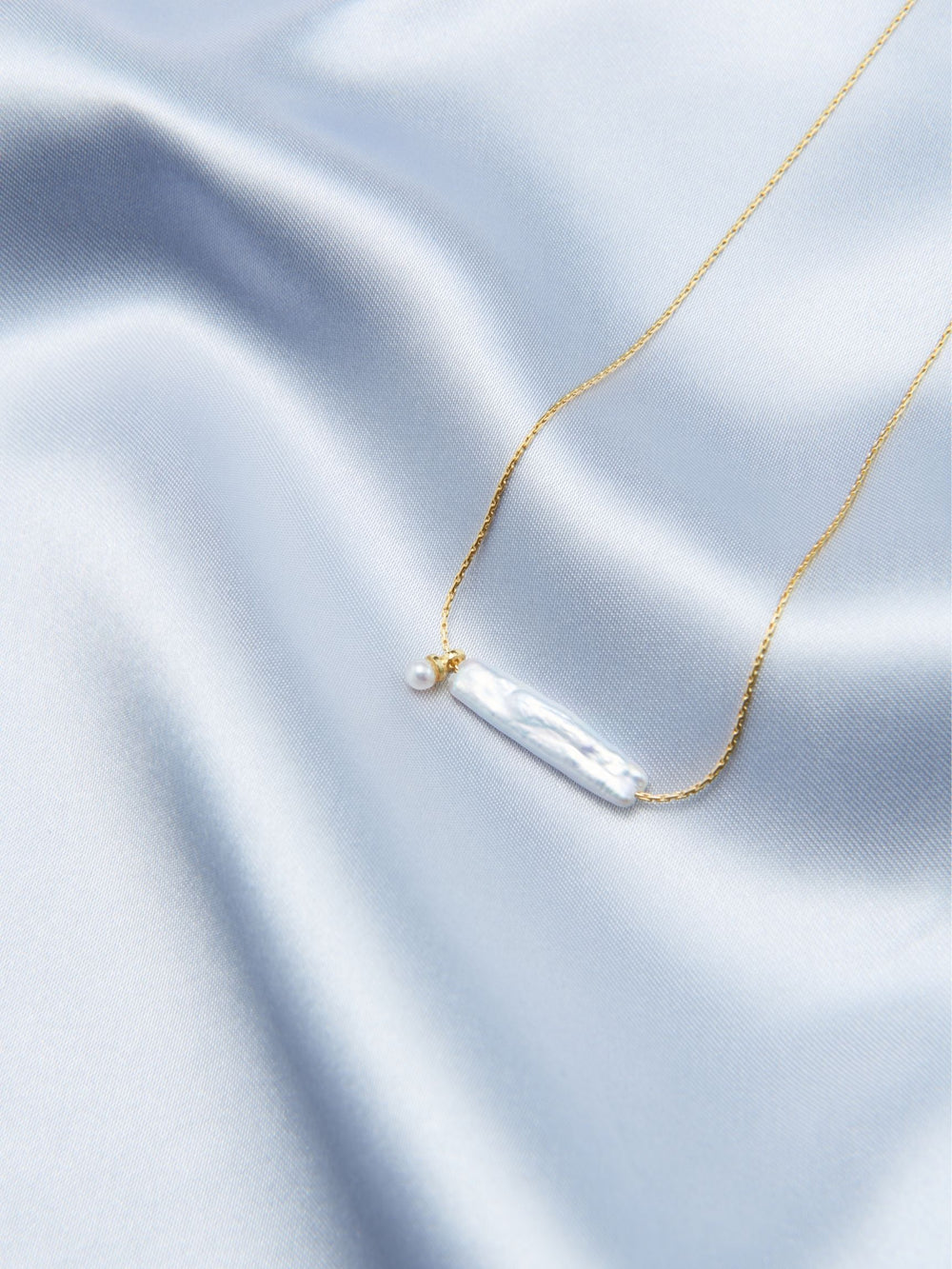 Elegant Pearl Necklace featuring a gold chain and a lustrous pearl detail on a soft satin background