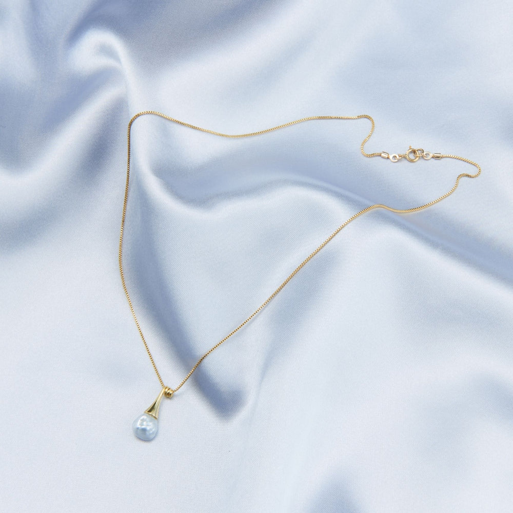 
                      
                        Elegant pearl pendant necklace on a soft blue satin background, featuring a delicate gold chain
                      
                    