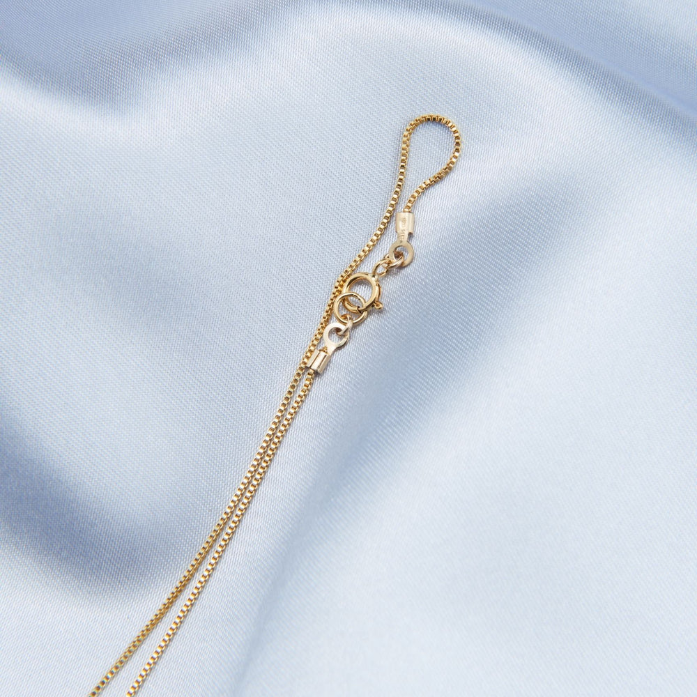 
                      
                        Close-up of an elegant pearl pendant necklace chain with a secure clasp on soft fabric
                      
                    