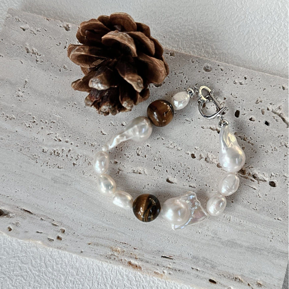 
                      
                        Handcrafted baroque bracelet featuring irregular pearls and a tiger's eye stone on a textured surface
                      
                    