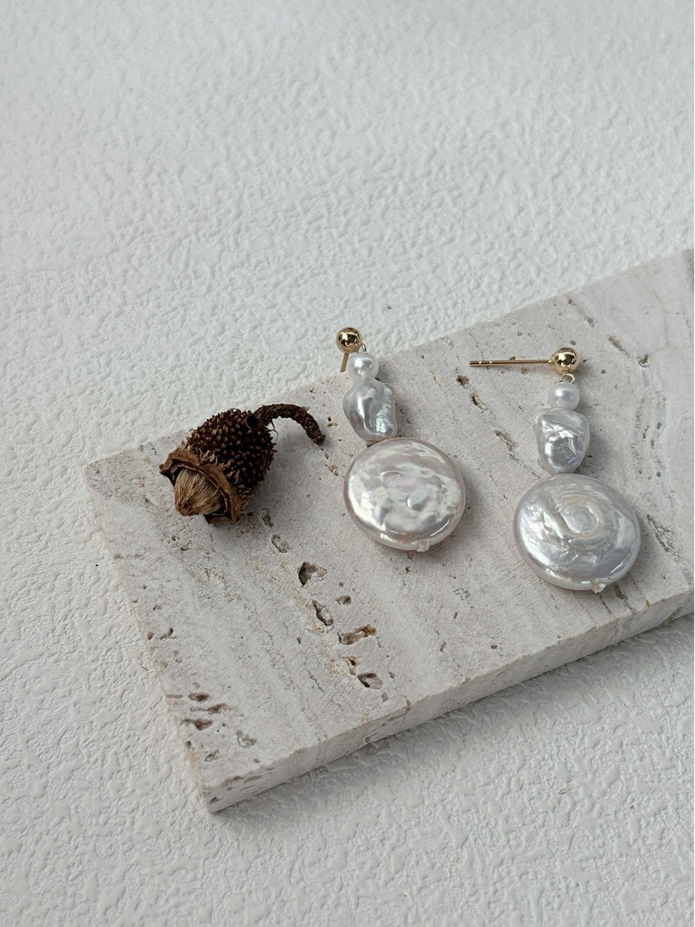 Handmade baroque earrings featuring unique pearl designs on a textured display