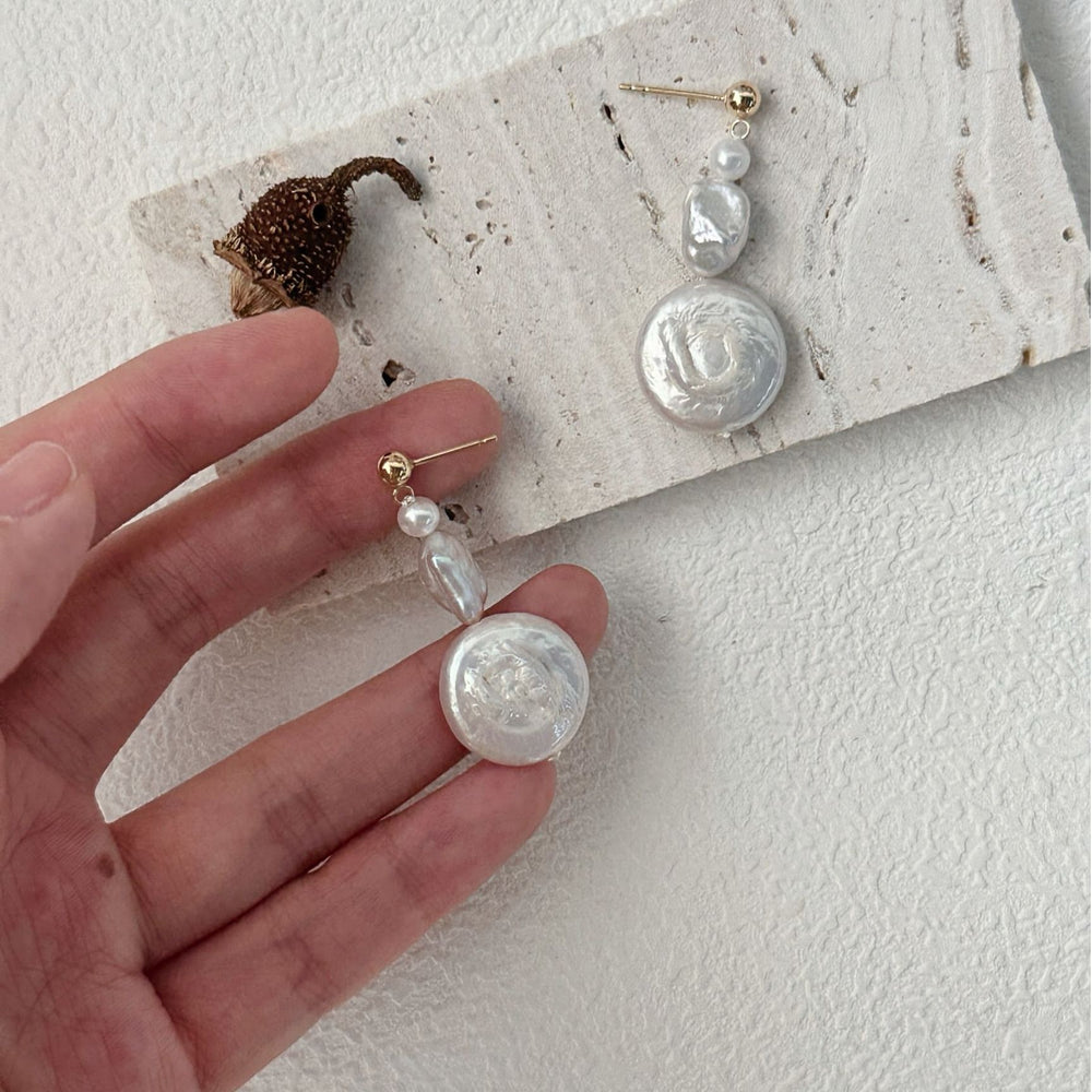 
                      
                        Handmade baroque earrings featuring unique pearl designs with gold accents on a textured display
                      
                    