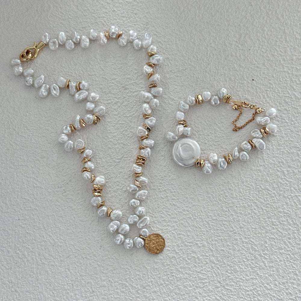 
                      
                        Handmade Keshi pearl necklace with golden accents alongside matching bracelet on a white surface
                      
                    