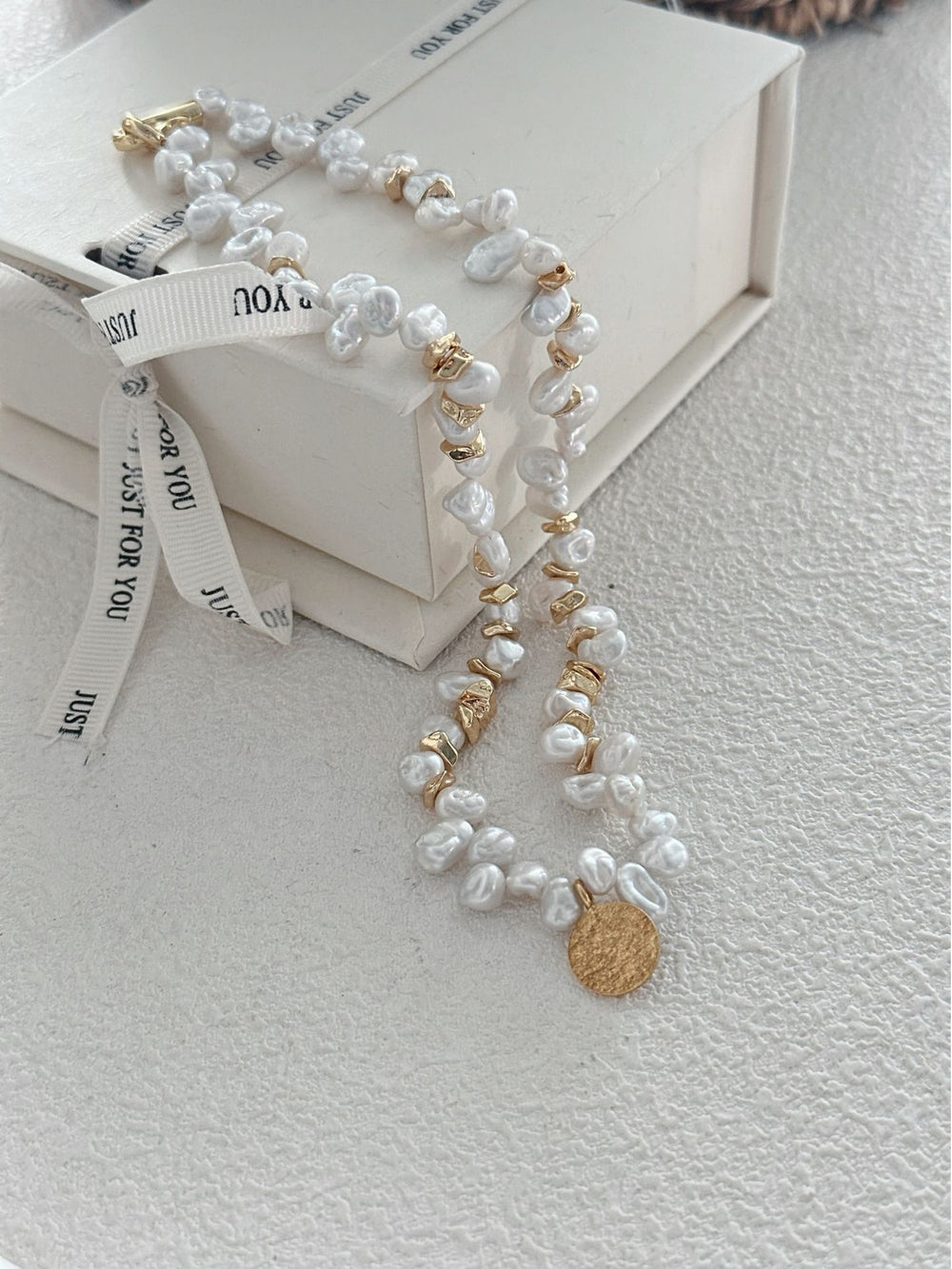 Handmade Keshi pearl necklace with gold accents and a textured pendant on a decorative background