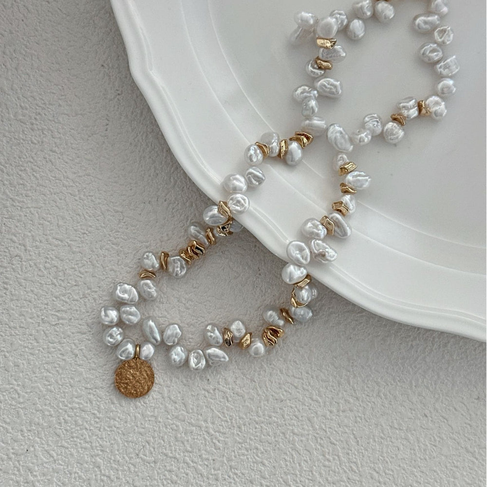 
                      
                        Handmade Keshi pearl necklace with gold accents on a white plate background
                      
                    