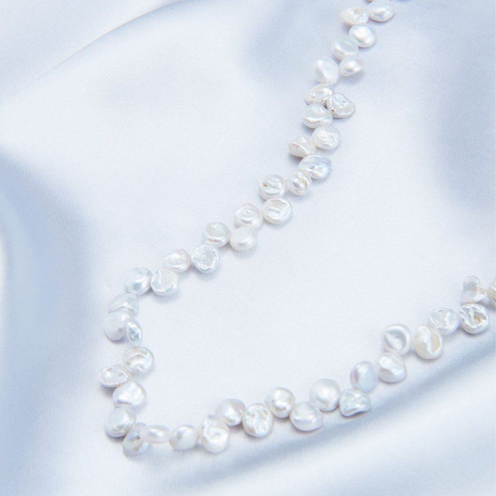 
                      
                        Handmade Keshi pearl strand necklace on soft silk fabric, showcasing unique organic shapes
                      
                    