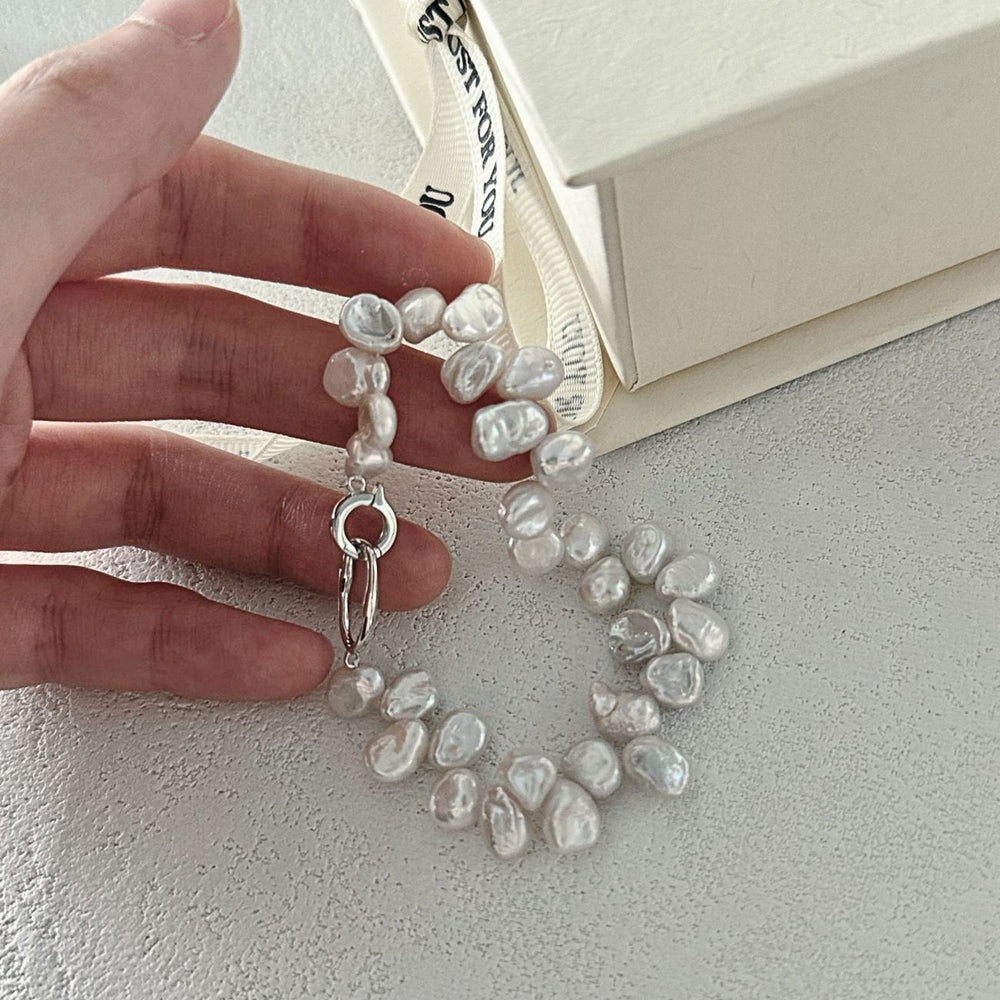 
                      
                        Close-up of a hand holding a Keshi pearl bracelet with a shiny silver clasp
                      
                    