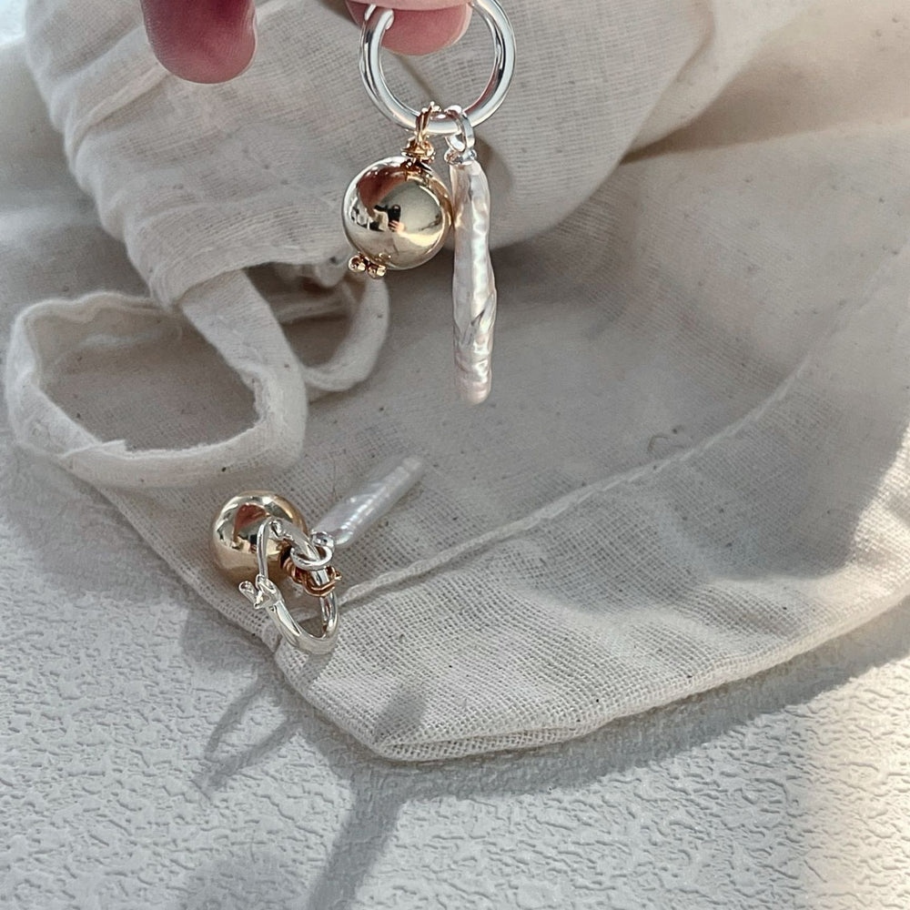 
                      
                        Elegant luxury gold pearl earrings featuring unique design elements with a soft fabric background
                      
                    