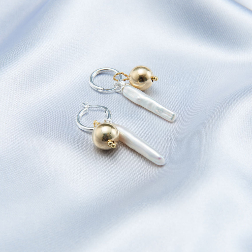 
                      
                        Luxury gold pearl earrings featuring a sleek design with elongated pearl and round gold accents
                      
                    