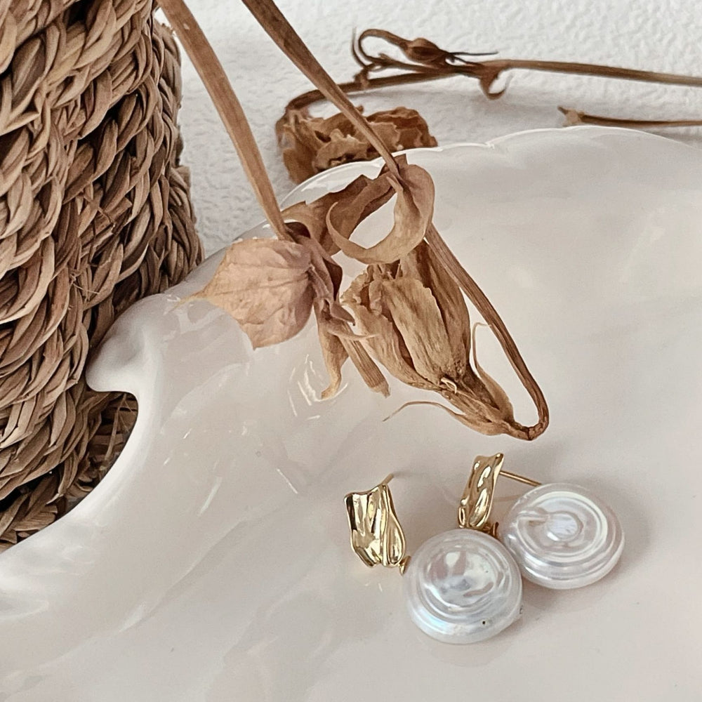 
                      
                        Stylish modern baroque earrings with unique pearl design and gold accents on a decorative plate
                      
                    