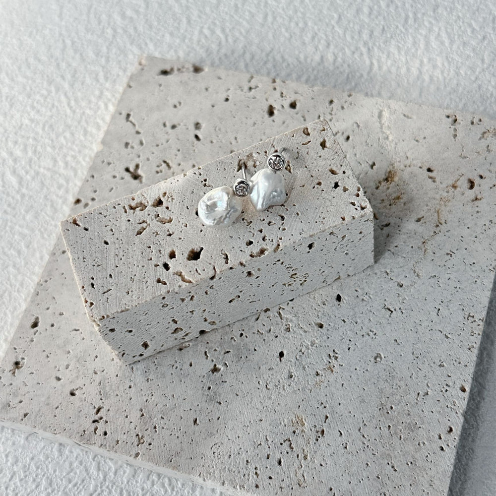 
                      
                        Natural keshi pearl earrings with unique shapes on a textured display surface
                      
                    