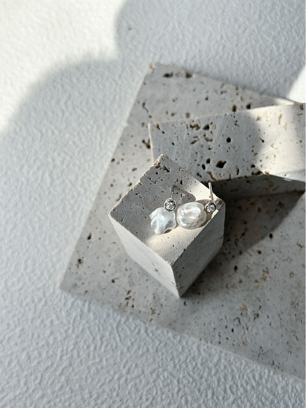 Elegant natural keshi pearl earrings with sparkling accents displayed on a textured surface