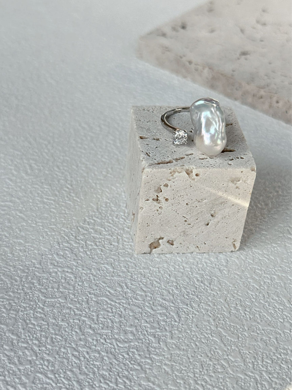 Elegant petite baroque pearl ring displayed on a stone stand, featuring a sparkling accent stone.