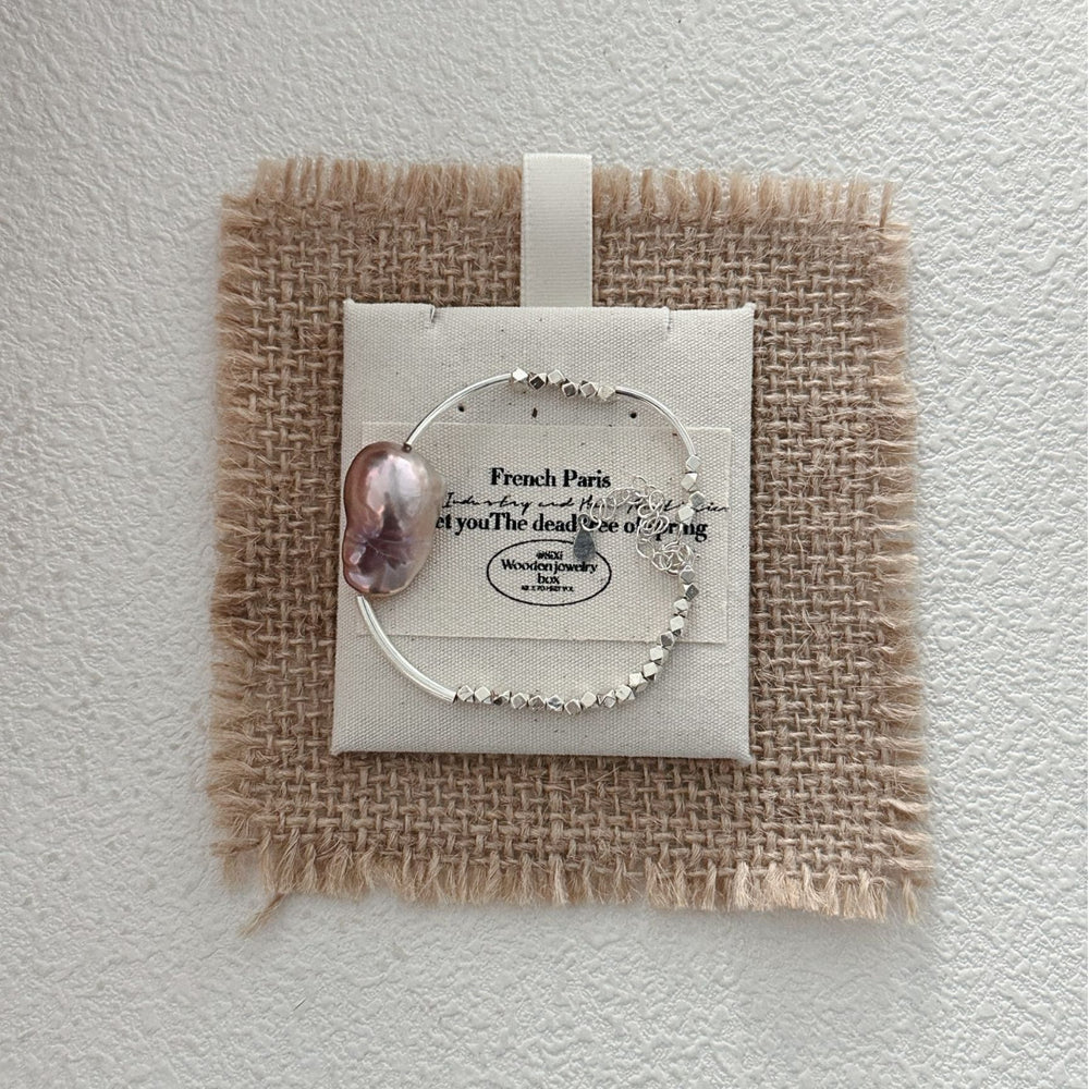 
                      
                        Elegant sterling silver pearl bracelet displayed on a textured burlap background
                      
                    