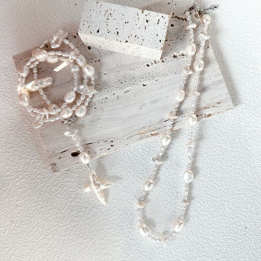 
                      
                        Elegant layered jewelry including a stylish baroque cross pendant and pearl bracelet displayed on a textured surface
                      
                    