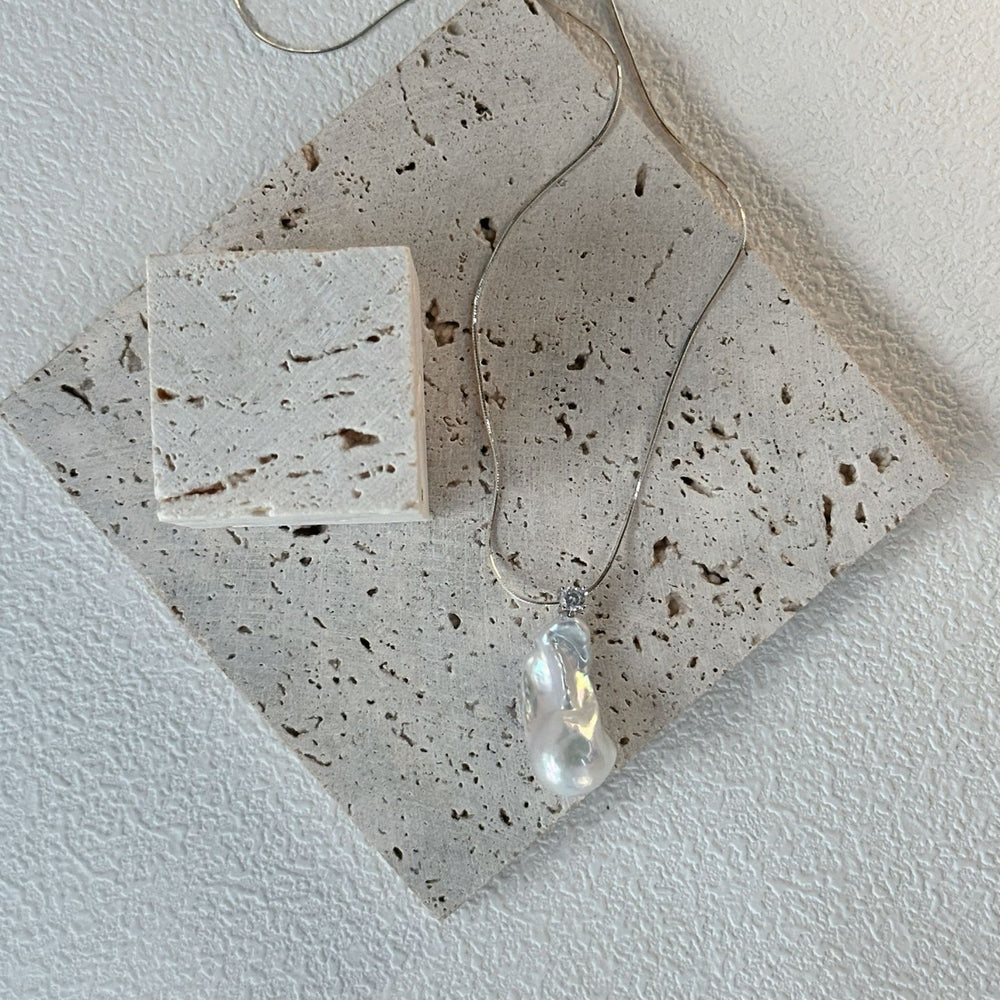 
                      
                        Unique baroque pearl necklace displayed on a textured surface with a minimalist design
                      
                    
