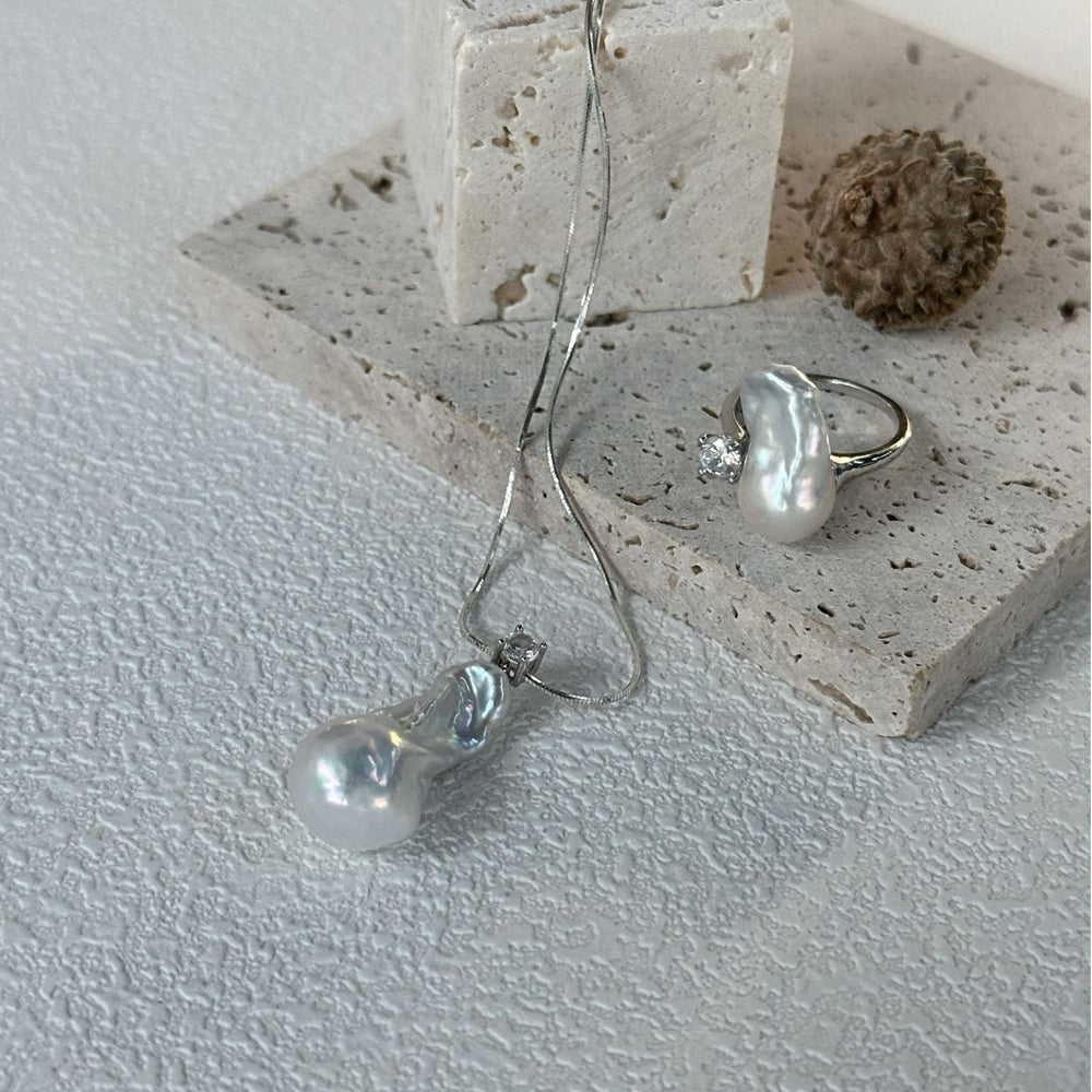 
                      
                        Unique baroque pearl necklace with a distinct shape, paired with matching earrings on a textured surface
                      
                    