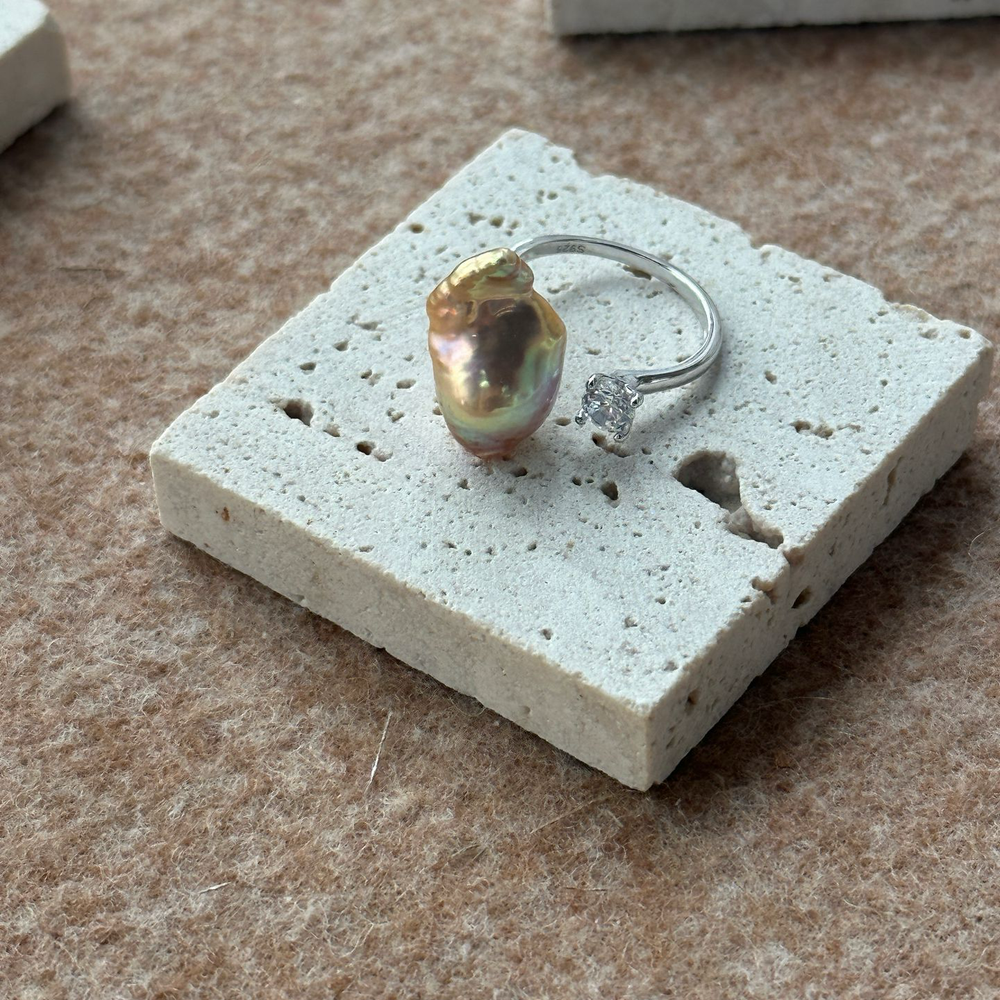 Unique baroque pearl ring set on a textured surface with a delicate silver band
