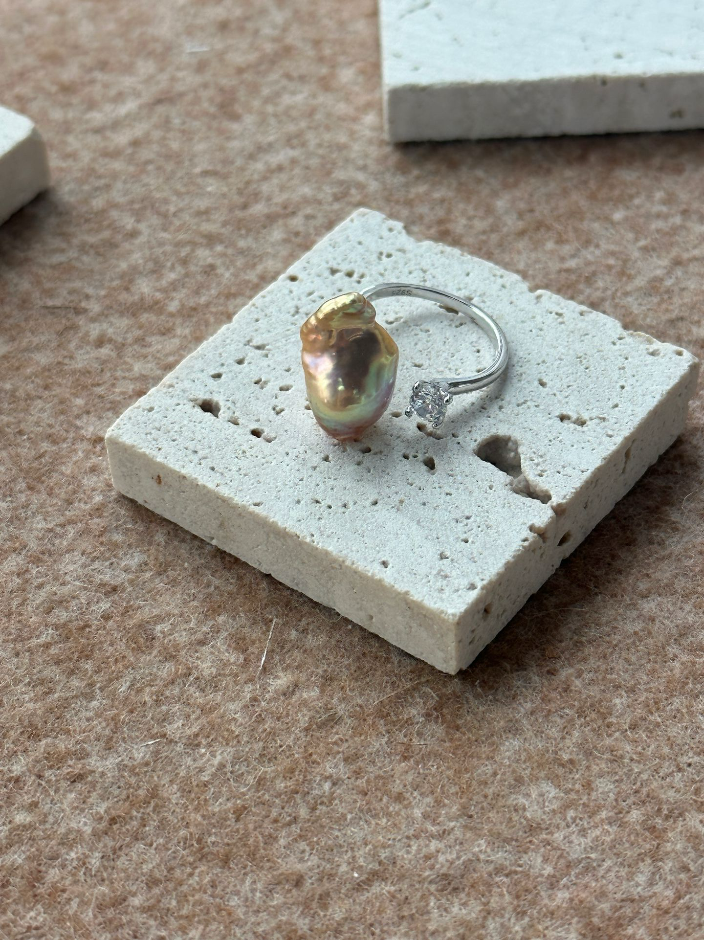 Unique baroque pearl ring set on a textured surface with a delicate silver band