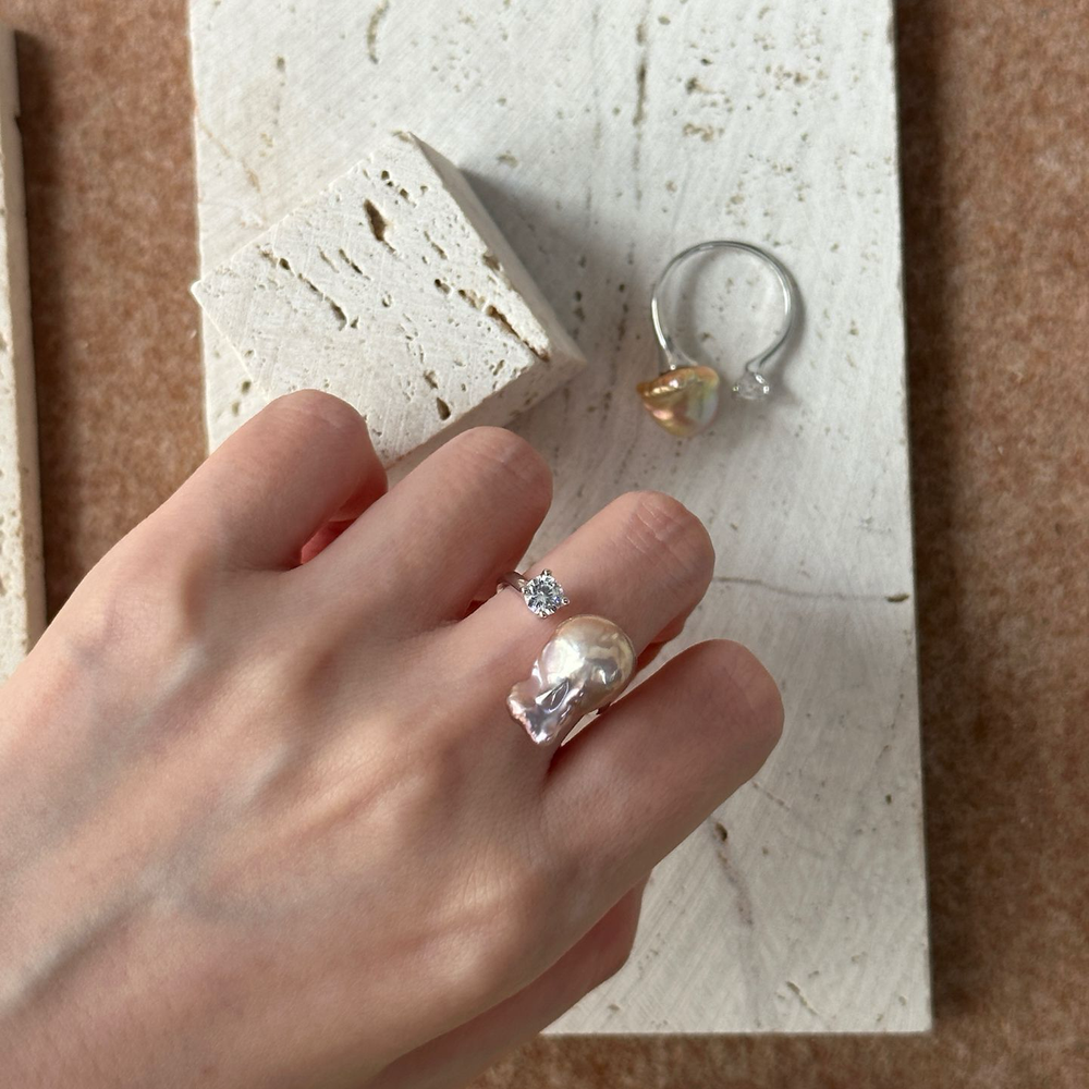 Elegant hand wearing a unique baroque pearl ring paired with minimalist silver accessories