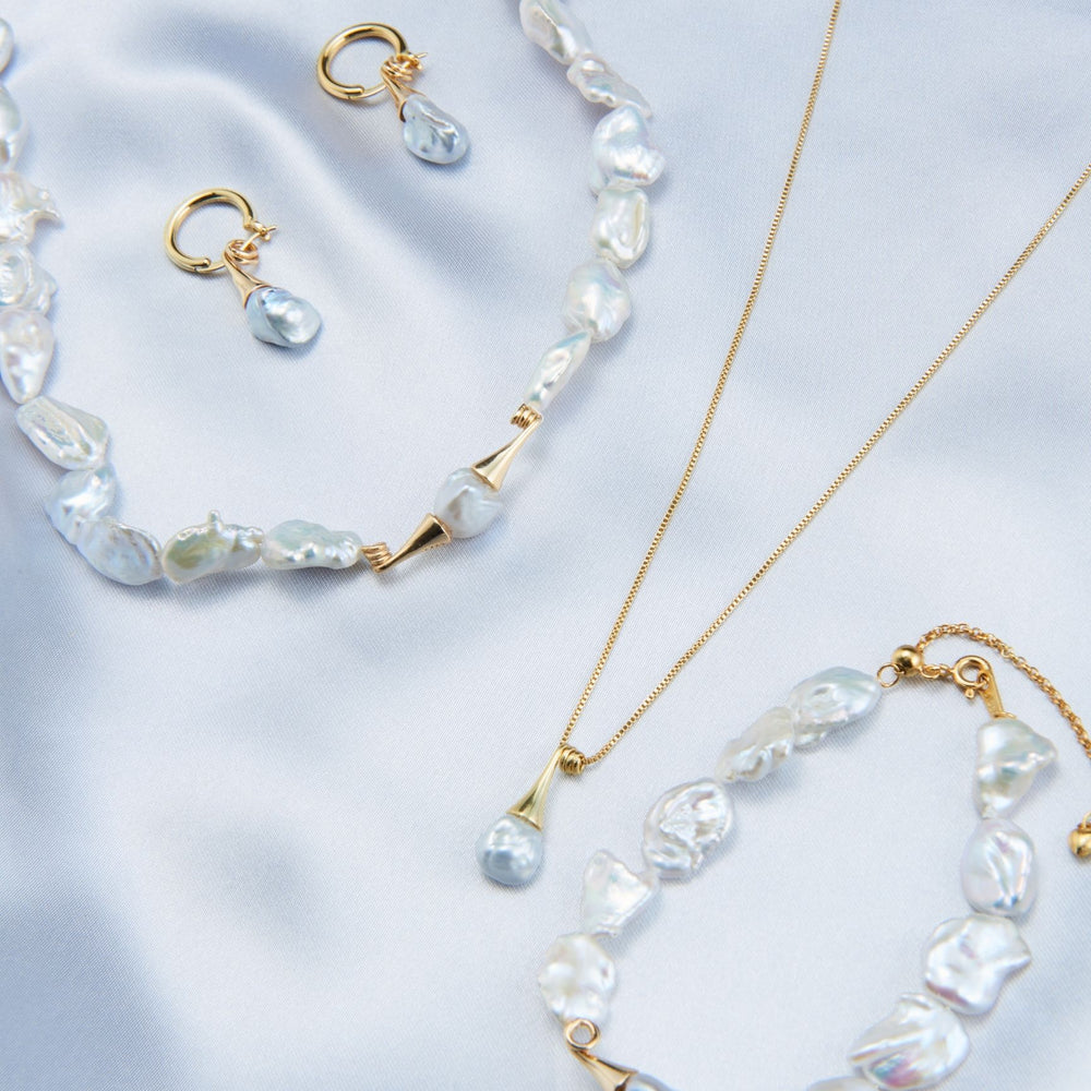 
                      
                        Unique pearl drop earrings with irregular shape, paired with matching pearl jewelry on soft satin background
                      
                    